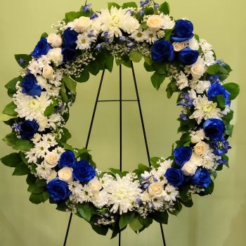 Heart-shaped floral wreath with blue and white flowers on a black stand