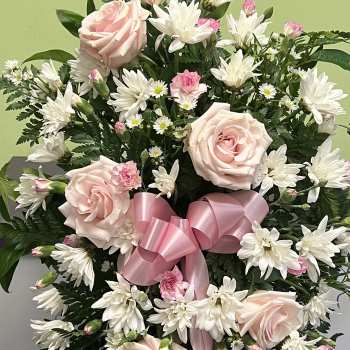 Pink roses and white daisies in a standing spray with a pink ribbon