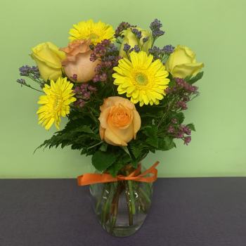 Yellow roses and gerbera daisies in a glass vase with an orange ribbon