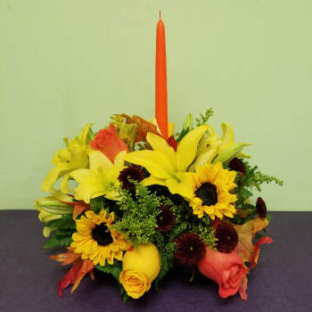 Yellow lilies and sunflowers arranged around a tall orange candle
