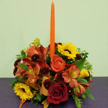 Autumn floral centerpiece with roses, sunflowers, and a tall orange candle