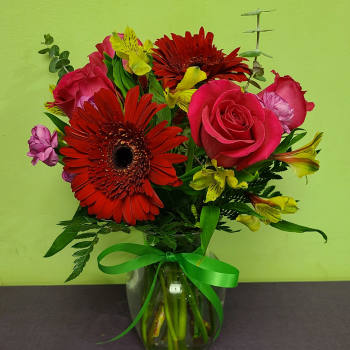 Bouquet of red gerbera daisies, pink roses, and yellow alstroemeria in a glass vase