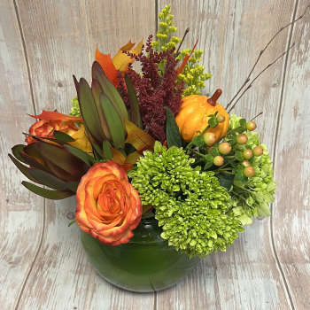 Orange rose arrangement in a green vase with pumpkins and autumn foliage