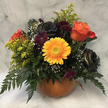 Autumn floral arrangement in a pumpkin-shaped container with roses and a yellow gerbera daisy