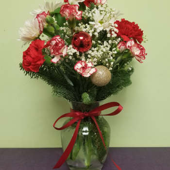 Red and white floral arrangement in a glass vase with holiday ornaments