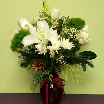 White lilies and roses arranged in a dark vase with a red ribbon