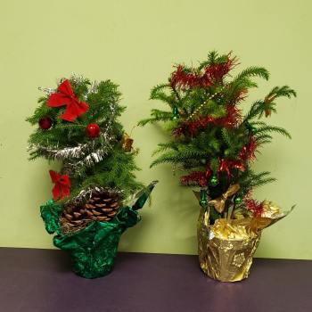 Two small decorated tabletop Christmas trees in foil pots