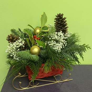 Holiday arrangement in a red basket with pinecones, white filler flowers, and gold ornaments