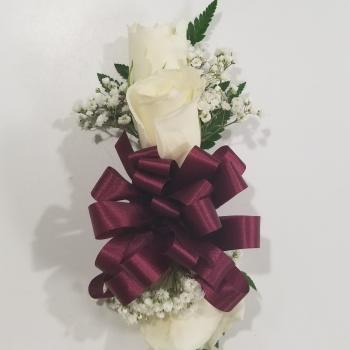 White rose corsage with baby's breath and a burgundy ribbon