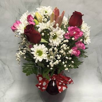 Bouquet of red roses, pink carnations, and white daisies in a dark vase