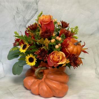 Fall floral arrangement in a pumpkin-shaped container with orange roses and sunflowers