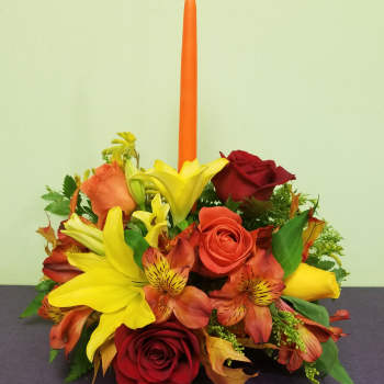 Red and yellow floral arrangement with a tall orange candle
