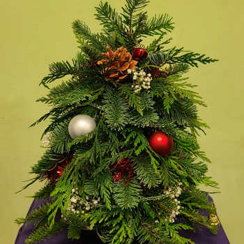 Small evergreen arrangement decorated with ornaments and a pinecone