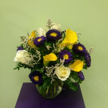 Bouquet of purple daisies, yellow calla lilies, and white roses in a glass vase