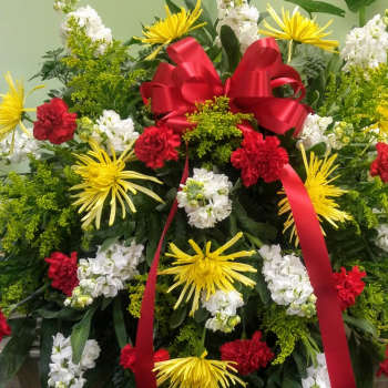 Large standing floral spray with red ribbon and yellow, white, and red flowers