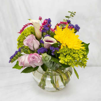 Mixed bouquet of roses, calla lilies, and chrysanthemums in a glass bowl vase
