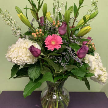 Mixed bouquet with lilies, roses, hydrangeas, and a pink gerbera in a glass vase