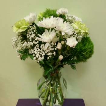 White flowers and green carnations arranged in a clear glass vase