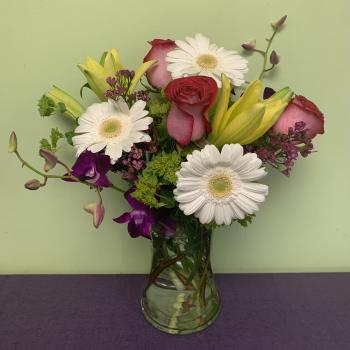 Mixed bouquet of roses, gerbera daisies, lilies, and orchids in a glass vase