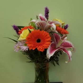 Mixed bouquet with orange gerbera daisies, pink lilies, and yellow roses in a glass vase