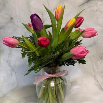 Mixed tulips in a clear glass vase with a pink ribbon