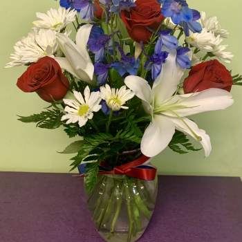 Bouquet of red roses, white lilies, blue flowers, and white daisies in a glass vase