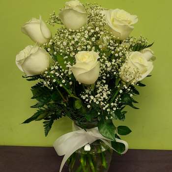 White roses and baby's breath in a glass vase with a white ribbon