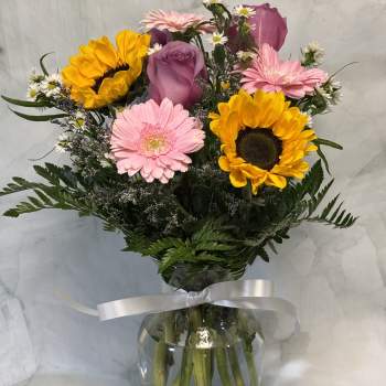 Mixed bouquet with sunflowers, pink gerberas, and a purple rose in a glass vase