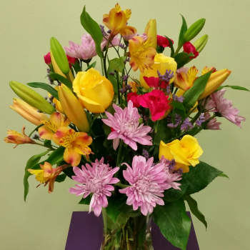 Mixed bouquet of yellow roses, lilies, and pink chrysanthemums in a glass vase