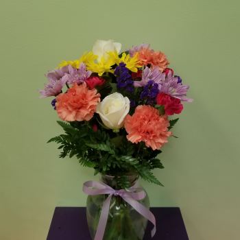 Mixed bouquet of carnations, daisies, and roses in a glass vase with a ribbon