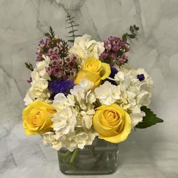 Yellow roses and white hydrangeas in a square glass vase