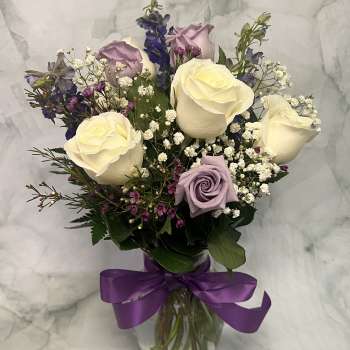 Bouquet of cream and lavender roses in a glass vase with a purple ribbon