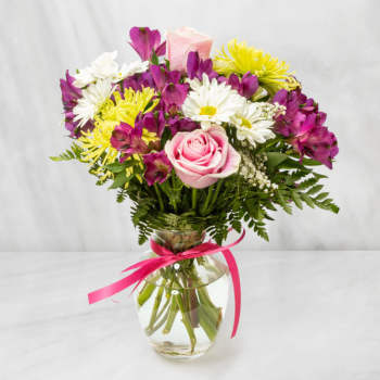 Mixed bouquet of pink roses, purple alstroemeria and white daisies in a clear vase with pink ribbon