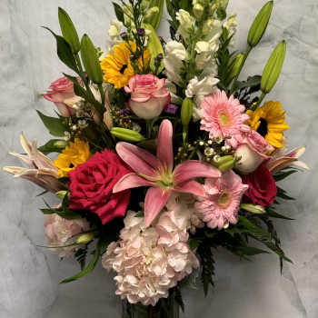 Mixed bouquet with pink roses, lilies, gerberas, sunflowers, and hydrangea in a glass vase