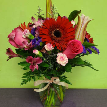 Mixed bouquet with pink roses, red gerbera daisies, and lilies in a glass vase