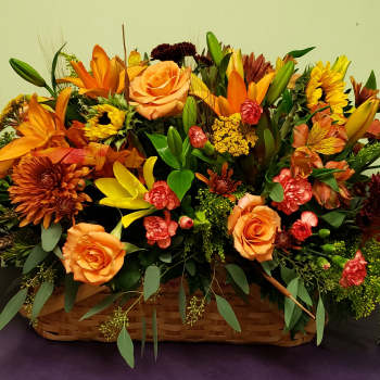 Basket arrangement of orange and yellow flowers with roses and lilies