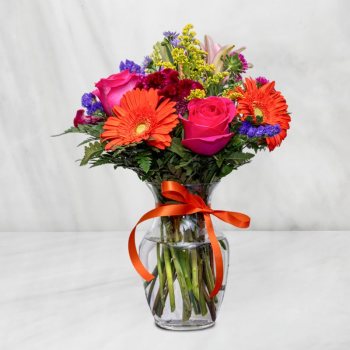 Mixed bouquet of bright flowers in a clear glass vase with an orange ribbon