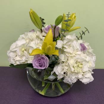 White hydrangeas with yellow lilies and lavender roses in a glass bowl vase