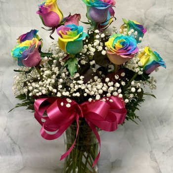 Rainbow-colored roses in a glass vase with a pink ribbon