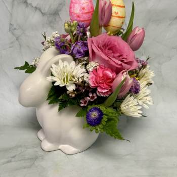 Pink and white floral arrangement in a white bunny container with decorative eggs
