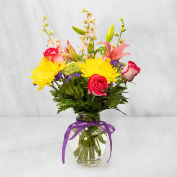 Mixed bouquet of roses, lilies, and yellow chrysanthemums in a glass vase