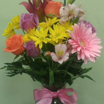 Mixed bouquet of roses, lilies, daisies, and alstroemeria in a glass vase with a pink ribbon