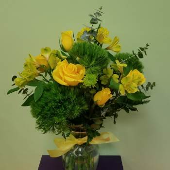 Yellow roses and alstroemeria in a glass vase with a yellow ribbon