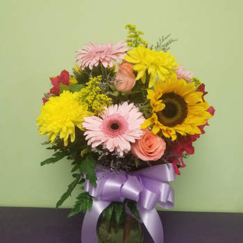 Mixed bouquet with sunflowers, pink gerberas, and roses in a glass vase