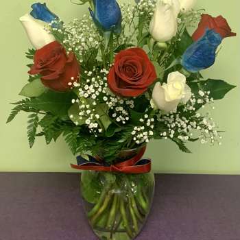 Red, white, and blue roses in a glass vase with baby's breath