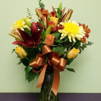 Mixed bouquet of lilies, roses, and daisies in a glass vase with a ribbon