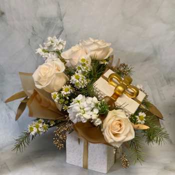 Cream roses and small white flowers arranged with a gift box and gold ribbon