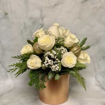 White roses arranged in a gold cylindrical vase with evergreen accents