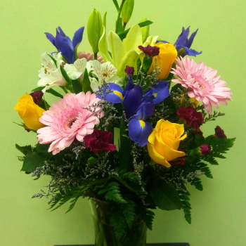 Mixed bouquet of lilies, roses, irises, and gerbera daisies in a glass vase