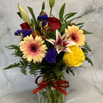 Mixed bouquet in a glass vase with lilies, roses, and gerbera daisies